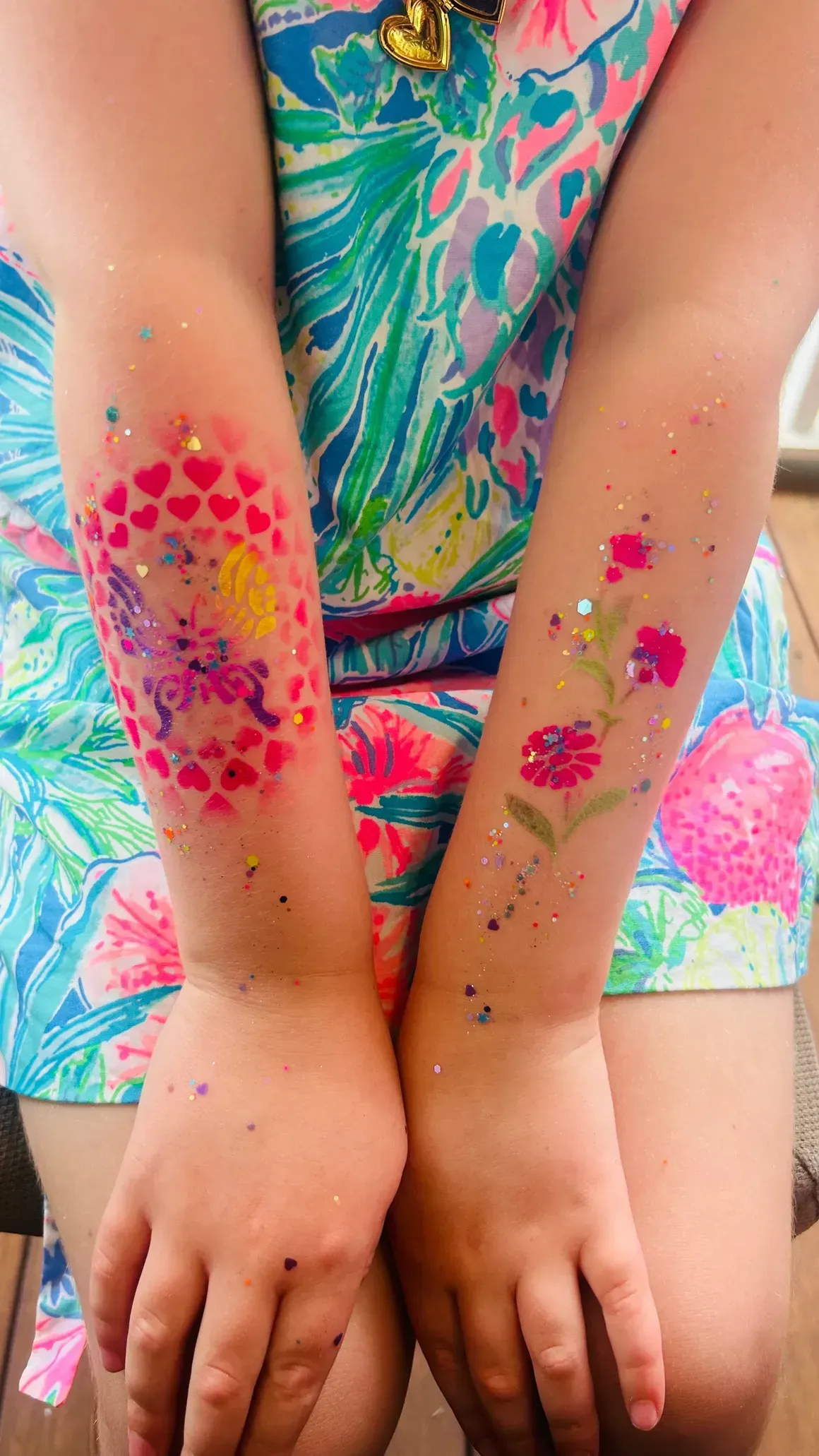 Arms decorated with glittery temporary tattoos: hearts and a unicorn on one, flowers on the other.