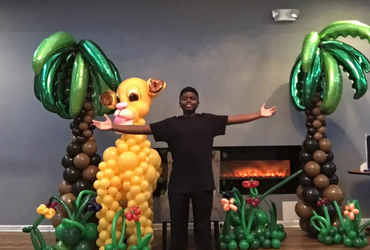 A man is standing in front of a lion made out of balloons.