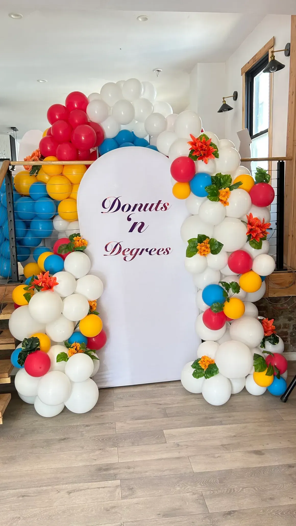 Colorful balloon archway with white sign, red, yellow, and blue accents, floral decorations.
