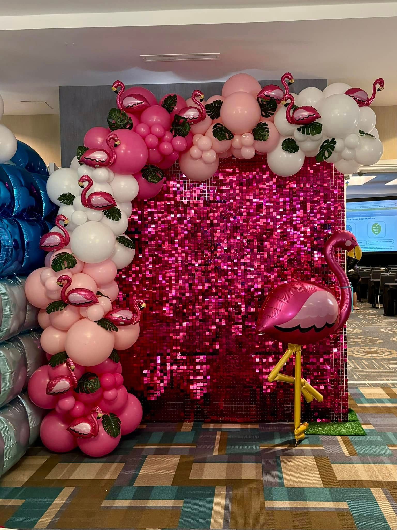 Pink and white balloon arch with flamingo decorations, beside a sequin wall and a flamingo balloon.
