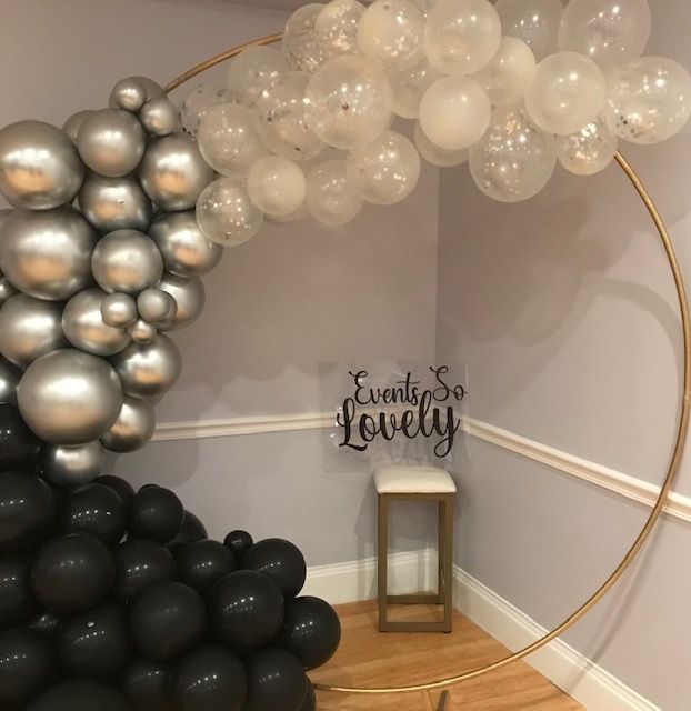 Gold hoop with black, silver, and clear balloons in corner. Sign that reads