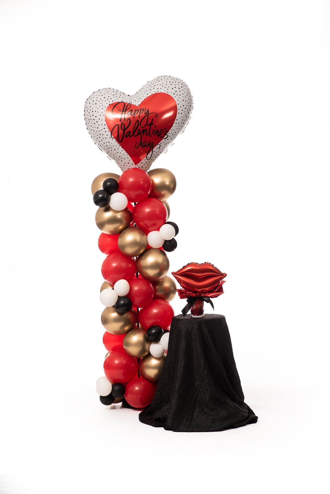 Balloon column with heart balloon, red and gold balloons, and a rose on a draped table.
