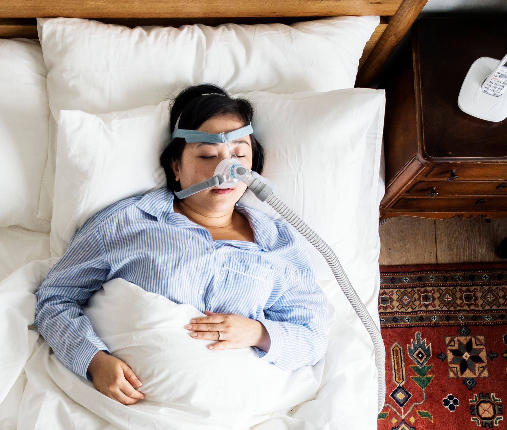 A woman is sleeping in a bed with an oxygen mask on her face.