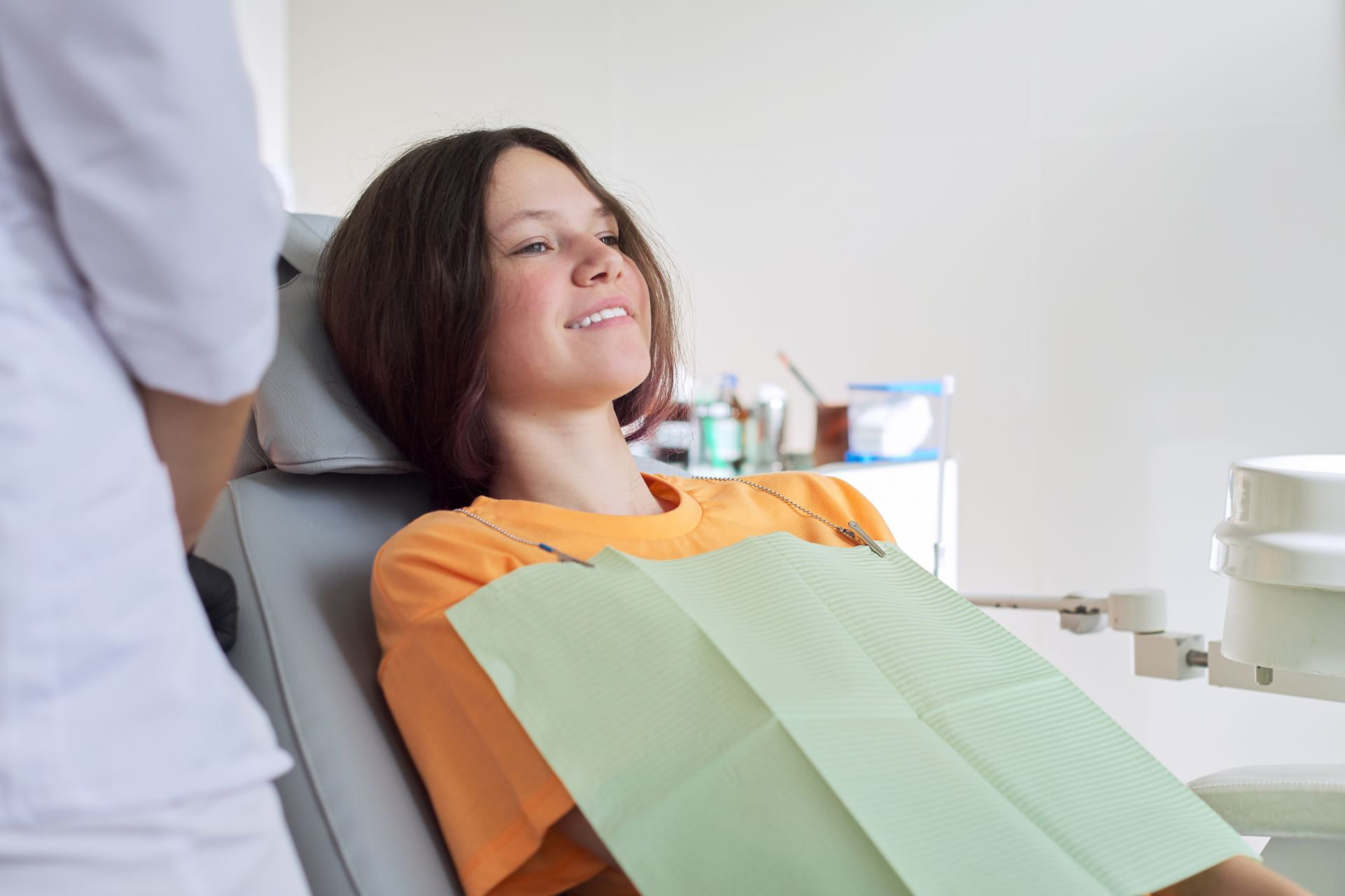 A young girl is sitting in a dental chair with her eyes closed.