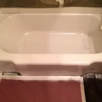 White bathtub beside a maroon floor mat in a bathroom