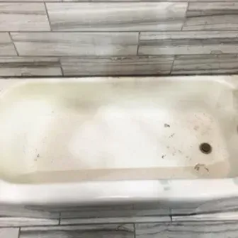 White bathtub with a dark drain and a small crack, set against tiled walls and floor.