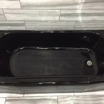 Black bathtub with a silver drain, viewed from above against light tile flooring