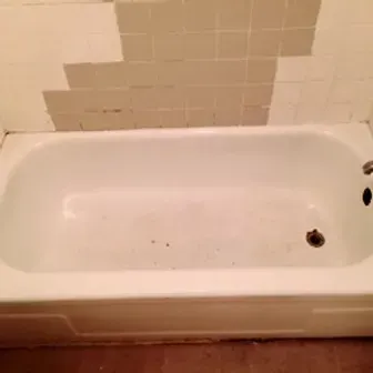 An empty white bathtub with beige tiled walls and some discoloration on the tiles.