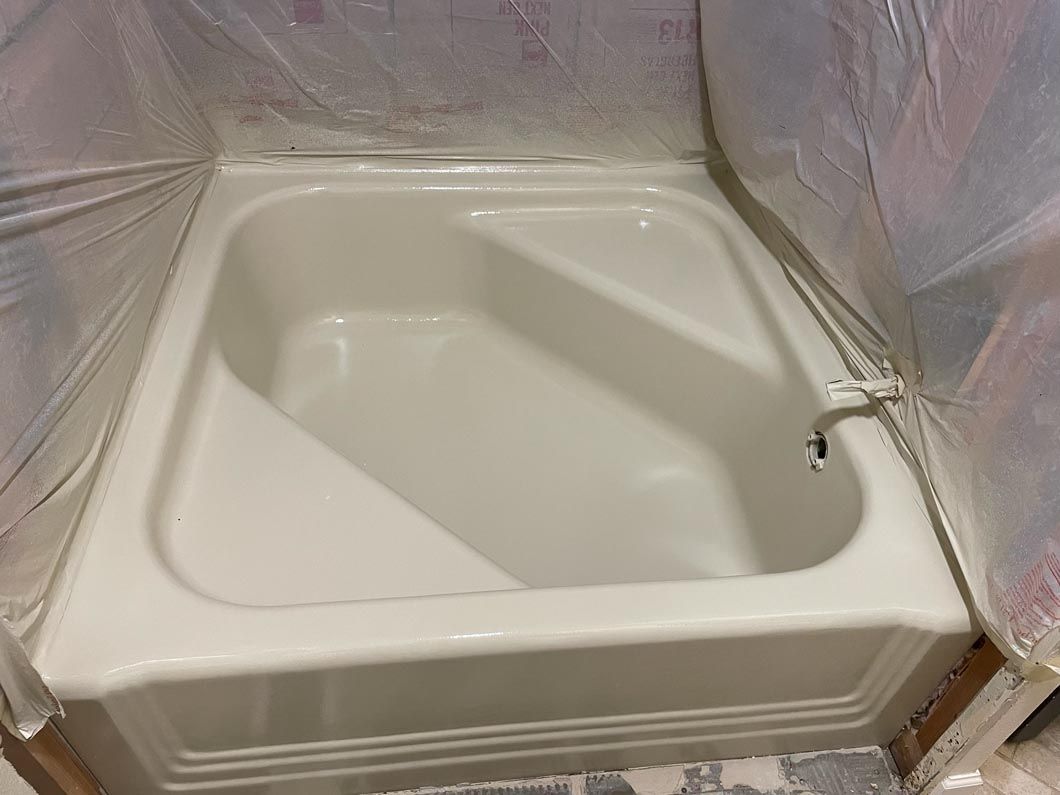 Small bathtub alcove being painted, with plastic sheeting and masking covering the walls.