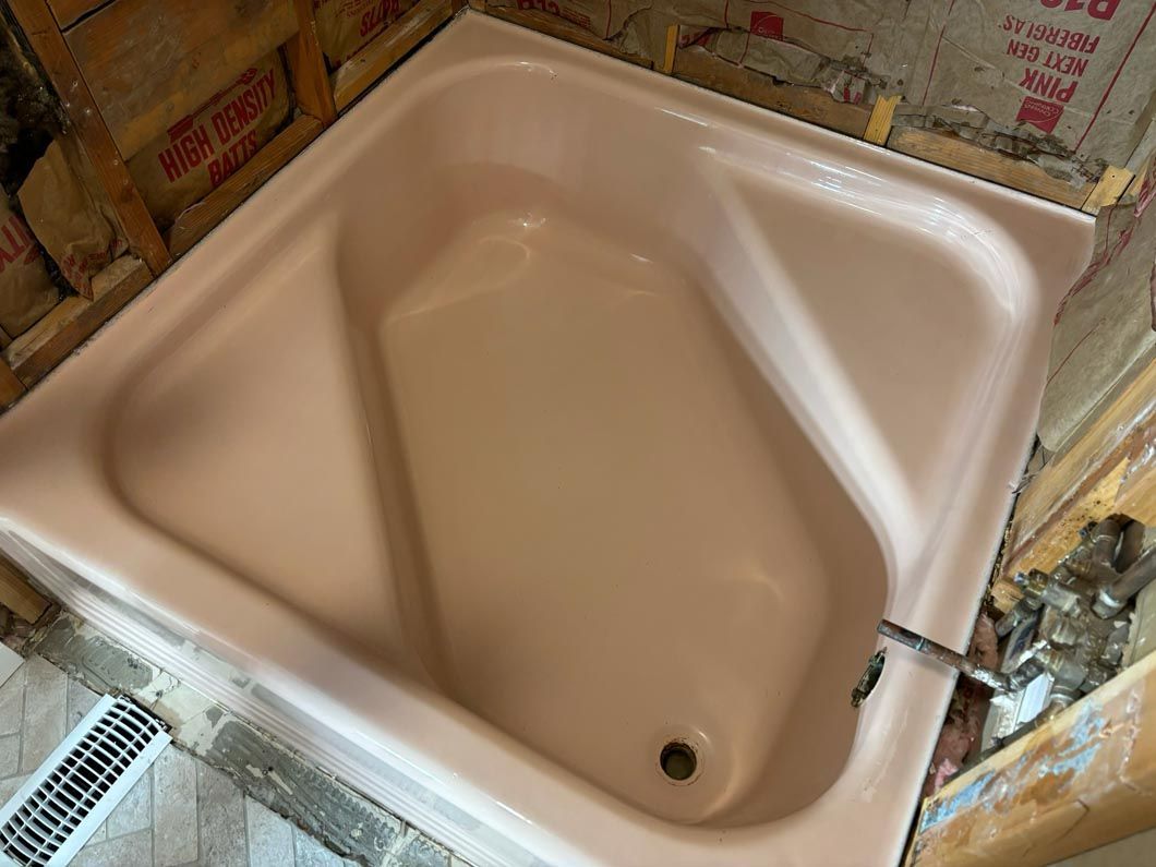 Beige bathtub in a bathroom under renovation, with exposed wall insulation and a shower hose on the right.