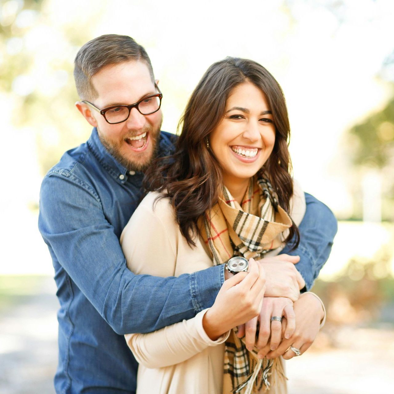A man wearing glasses is hugging a woman wearing a watch