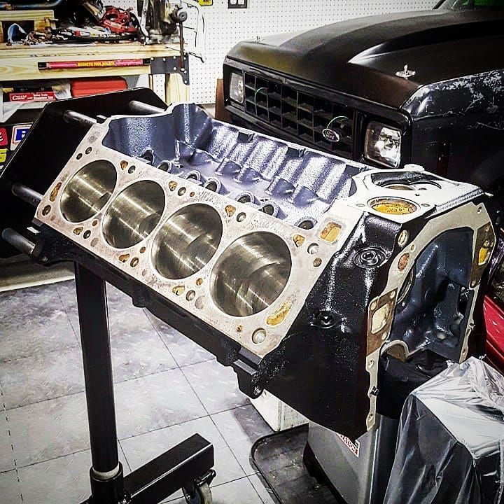 Engine block mounted on a stand, showing cylinder bores and machined surfaces, in a garage setting.