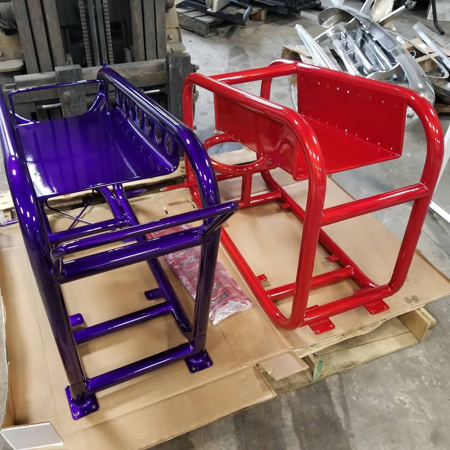 Two colorful metal frames, one purple, one red, on a pallet in a workshop setting.
