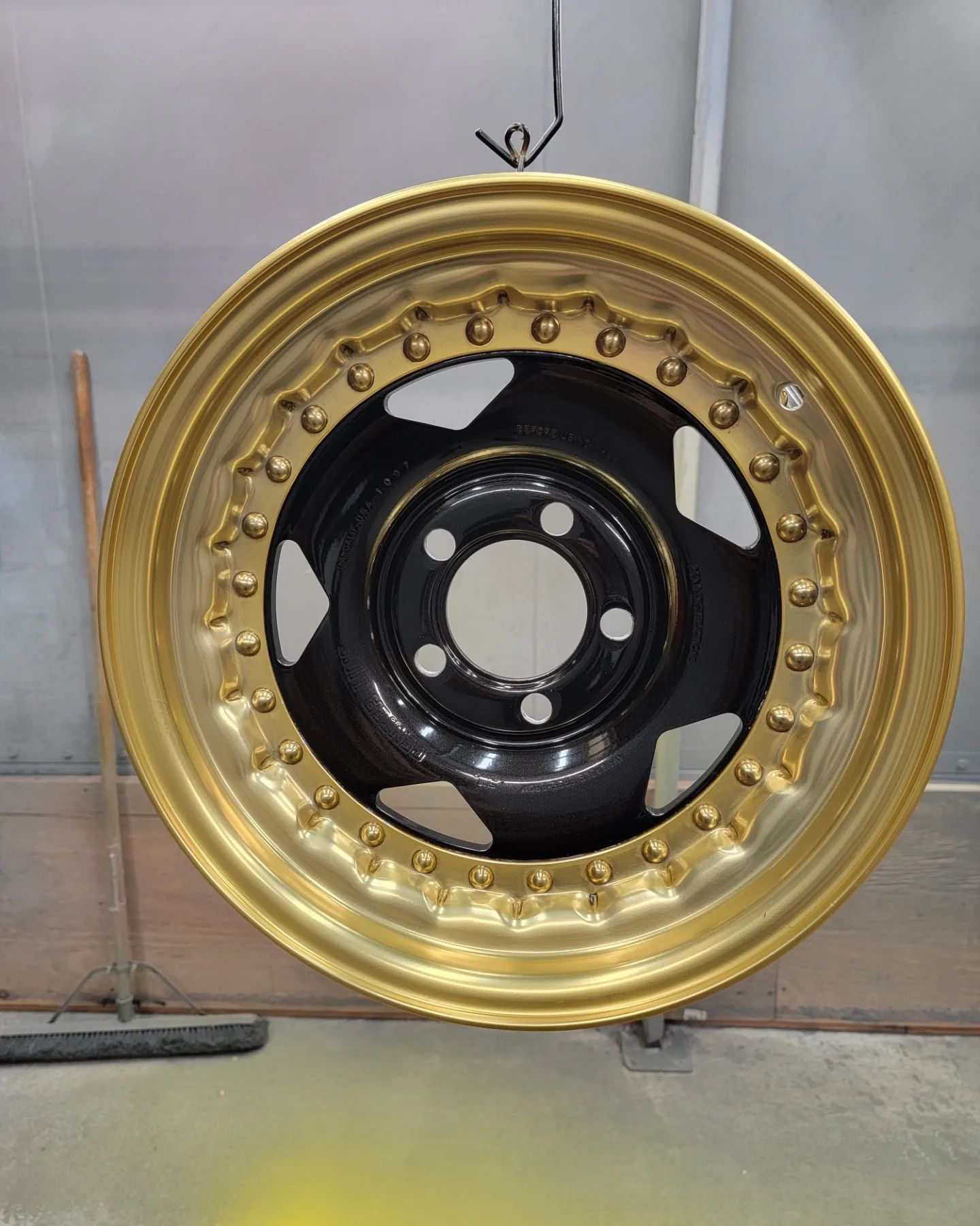Gold and black car rim hanging, freshly painted.