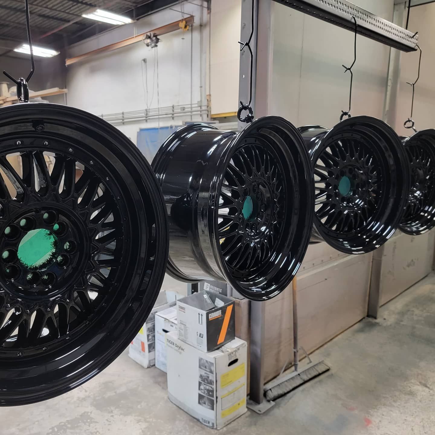 Black car rims hanging in a workshop, freshly painted with green center hubs.