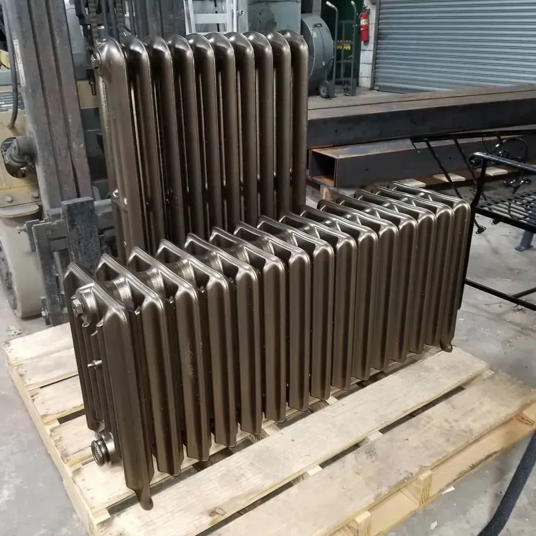 Three brown cast iron radiators stacked on a wooden pallet in a workshop.