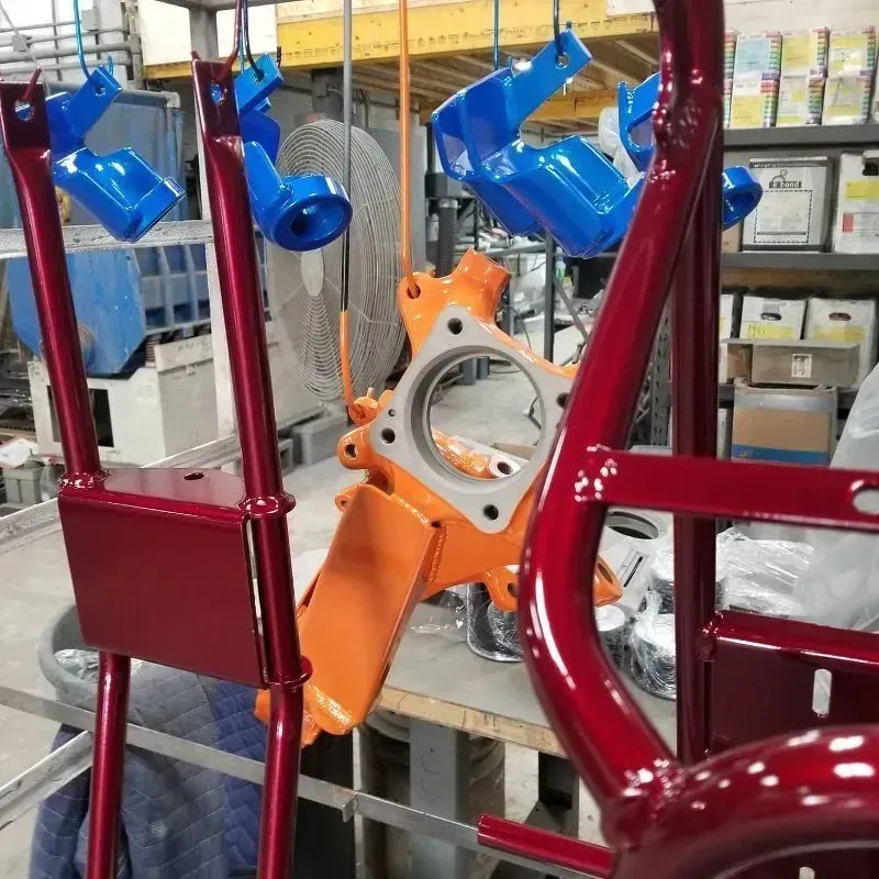 Metal parts, painted red, orange, and blue, hanging in a workshop, ready for assembly.