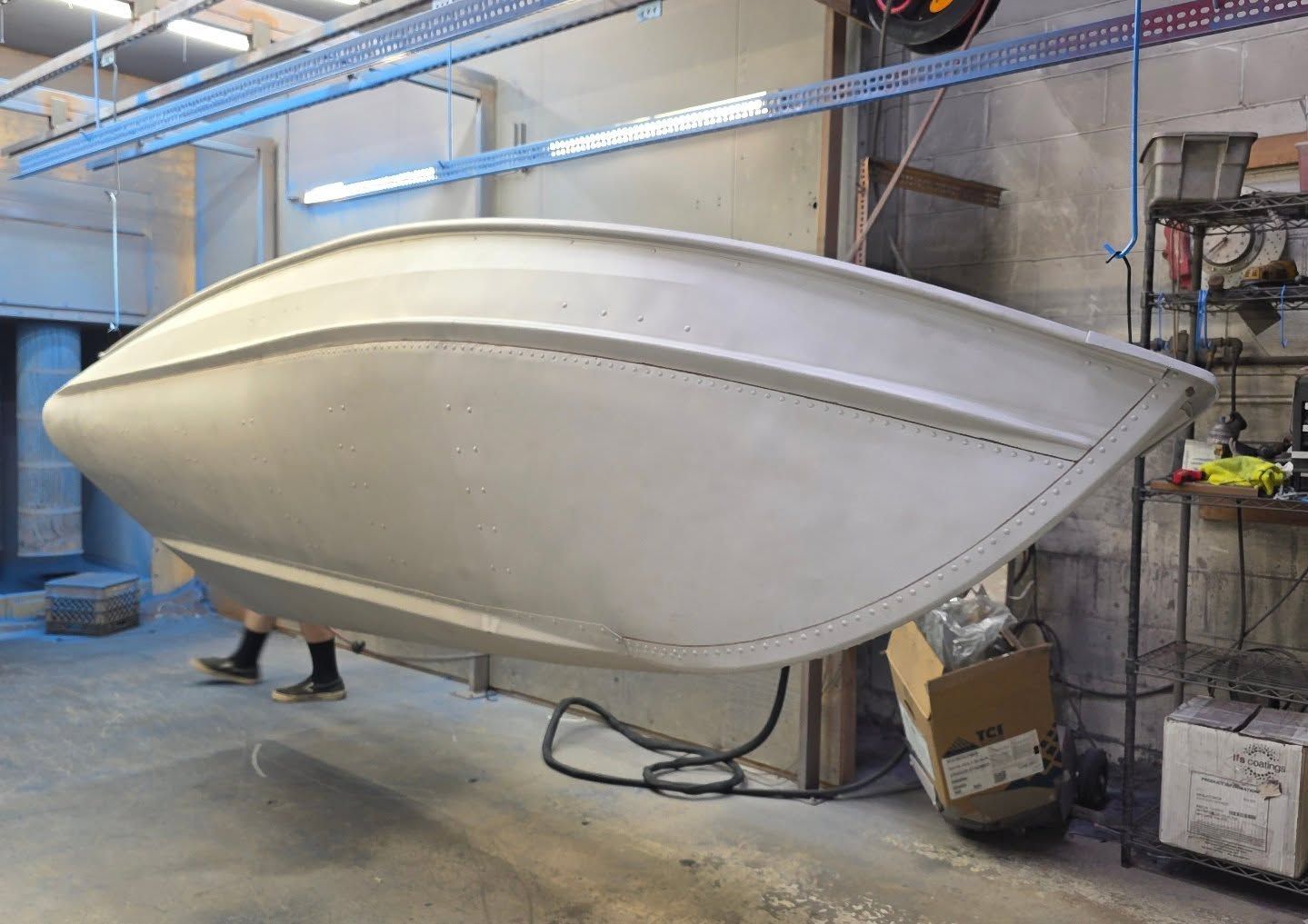 Aluminum boat hull suspended in a workshop.