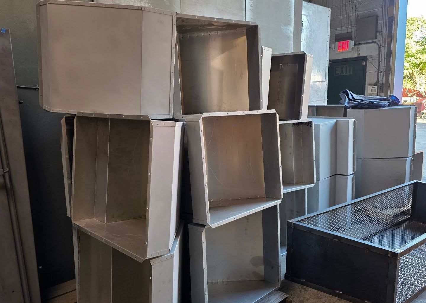 Metal rectangular ductwork components stacked in a warehouse setting.
