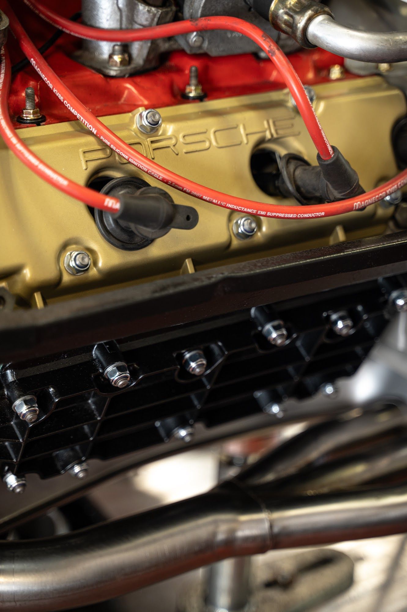 Close-up of a gold Porsche engine with red spark plug wires and black components.