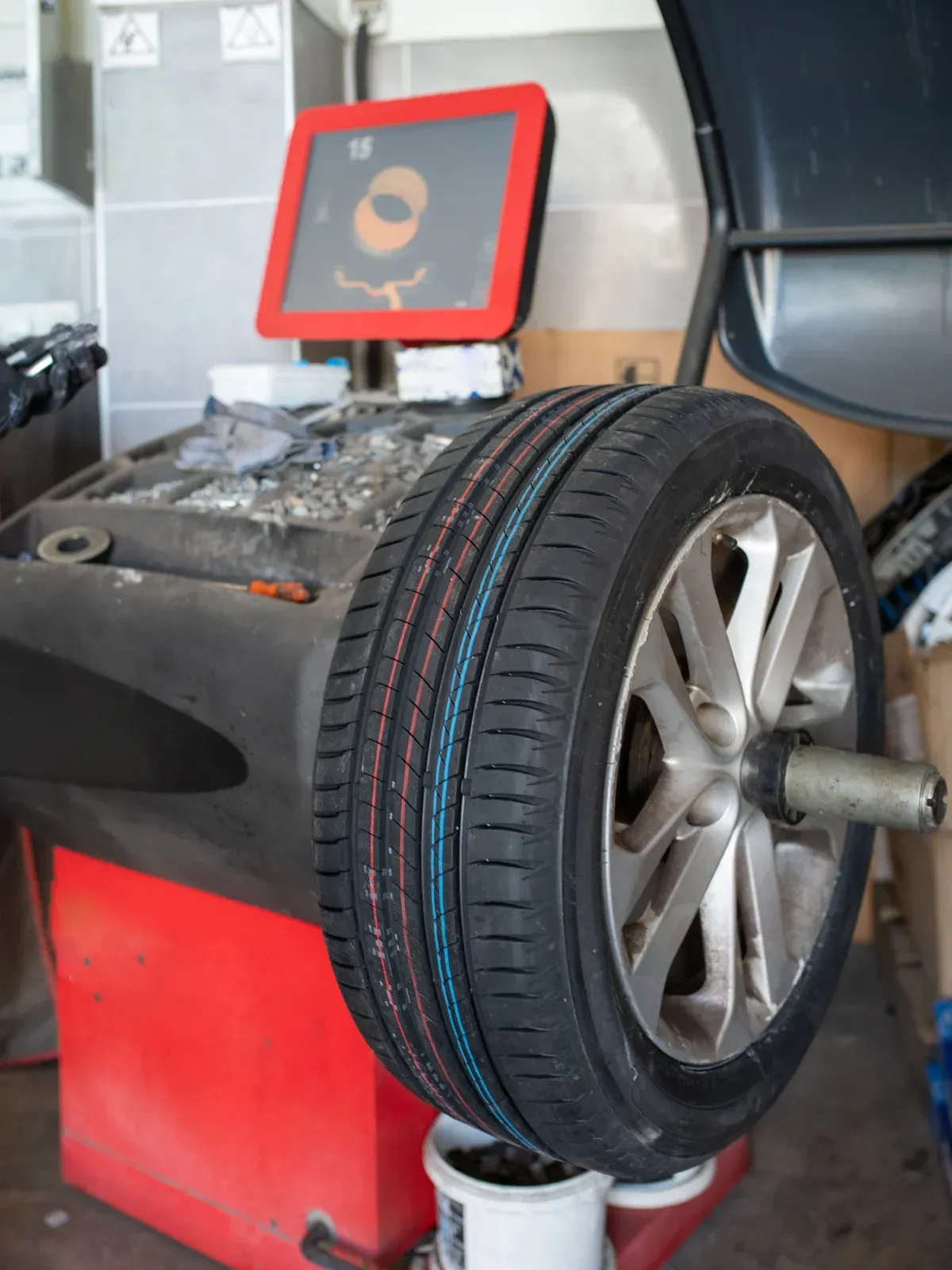 Tire balancing machine with a car tire mounted; red and black machine, gray wheel, tire with blue and red stripe.