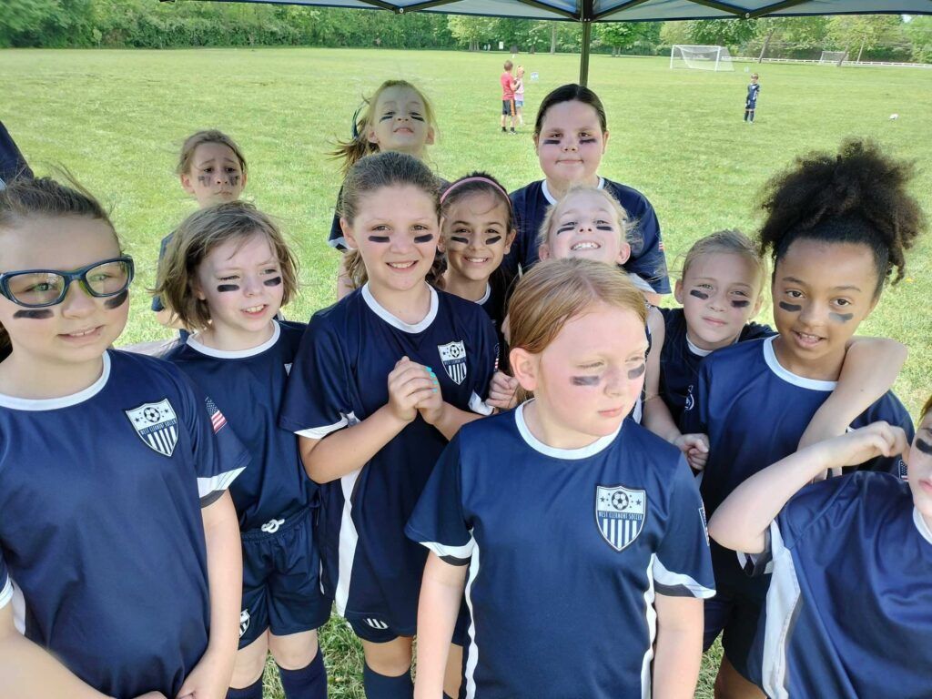 Children in navy shirts posing under a canopy at a park, with grass and other people in the background