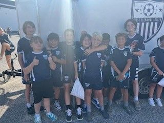 Youth soccer team posing in navy uniforms with a club banner outdoors