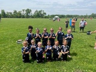 Youth sports team posing in a grassy field, holding medals after a game