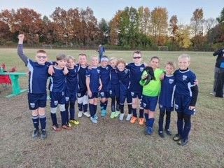 Youth soccer team in navy uniforms posing on a field, with trees in the background.