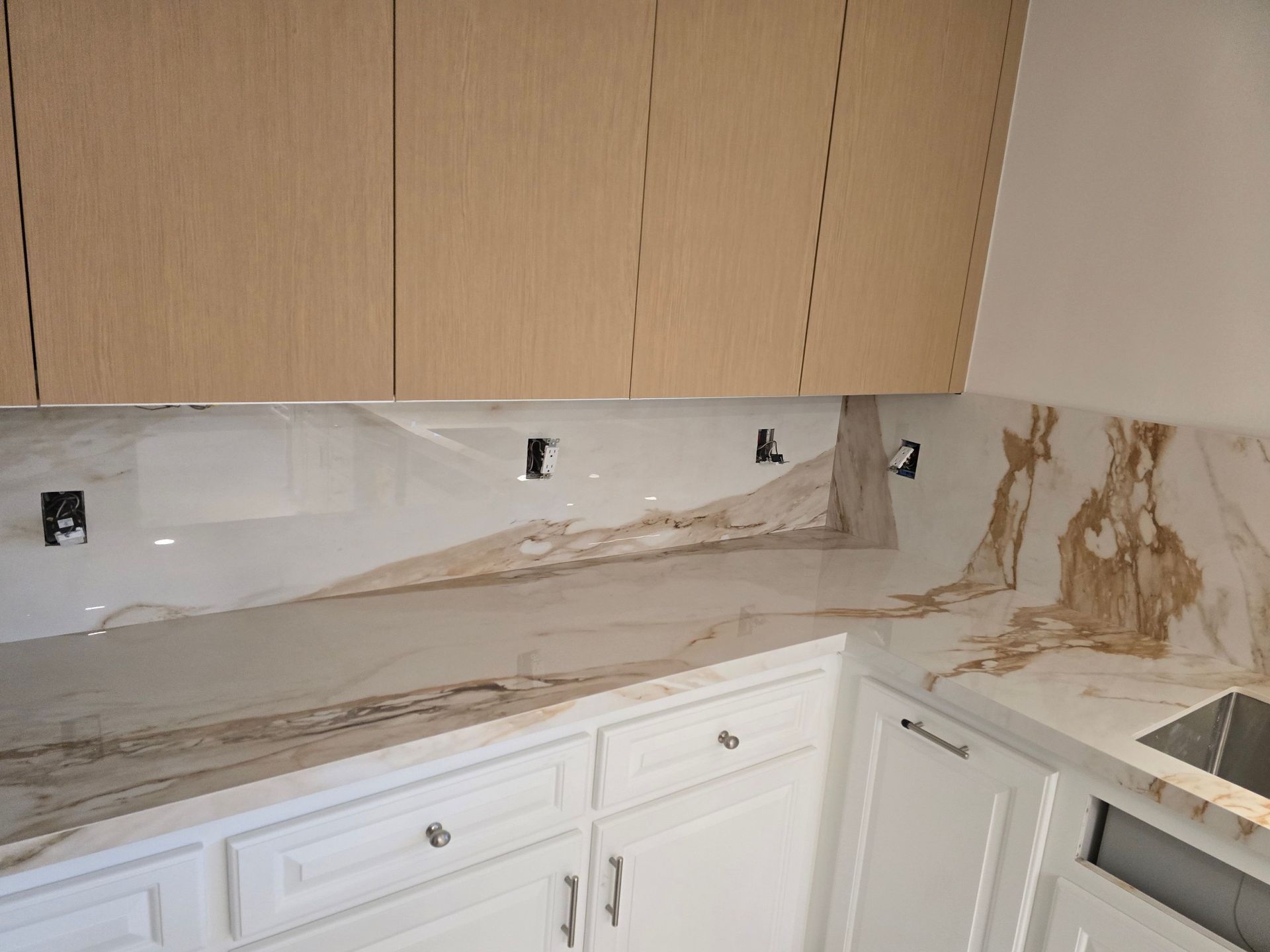 Kitchen with white cabinets, light wood uppers, and marble countertops with gold veining.