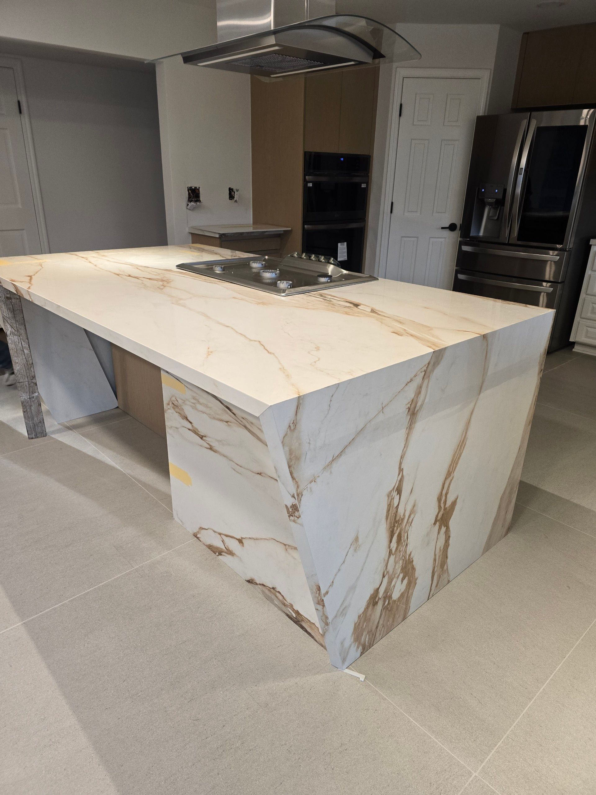 Kitchen island with white and gold marbled countertop and cabinets, awaiting finishing touches.