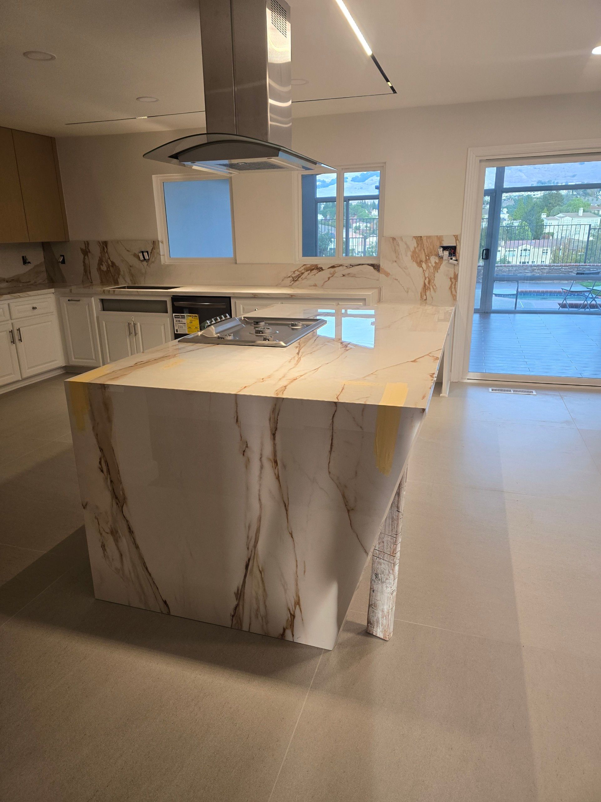 Kitchen with a marble island and range hood. Natural light from windows and open doorway.