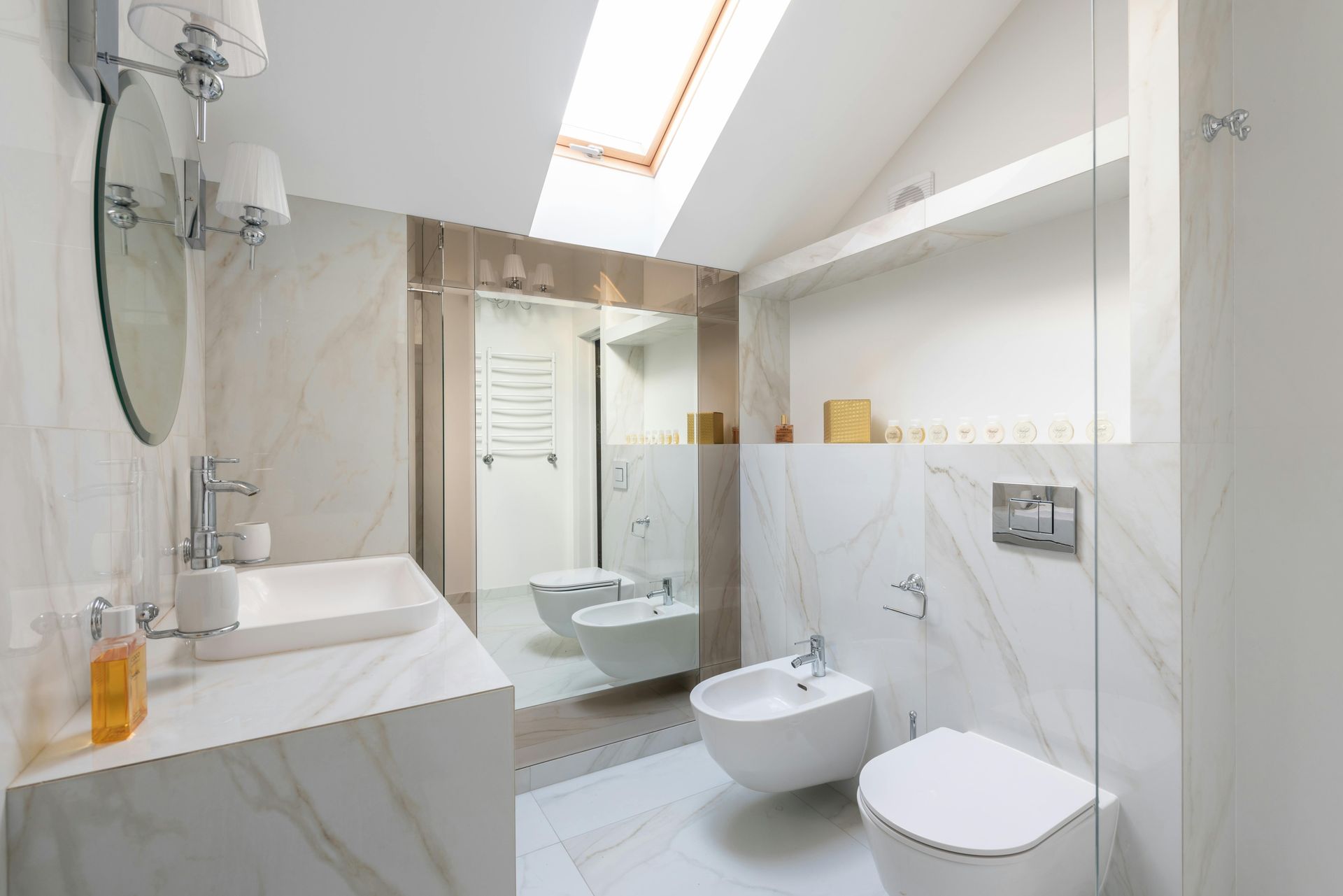 Modern bathroom with white marble walls, skylight, and white fixtures.