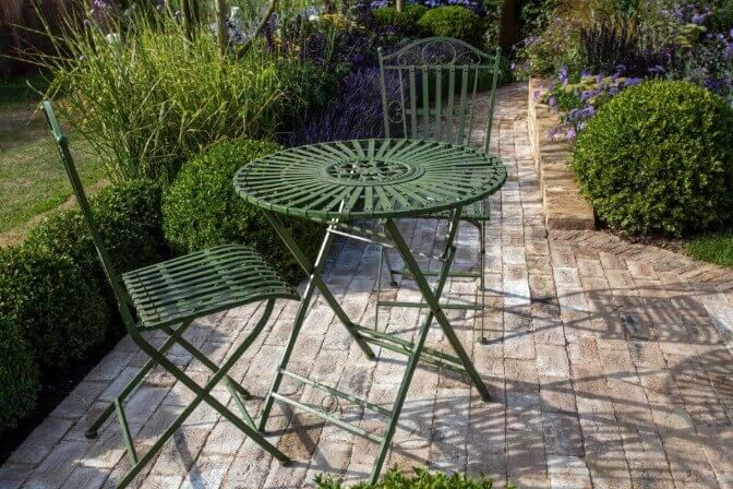 A green table and chairs are sitting on a patio in a garden.