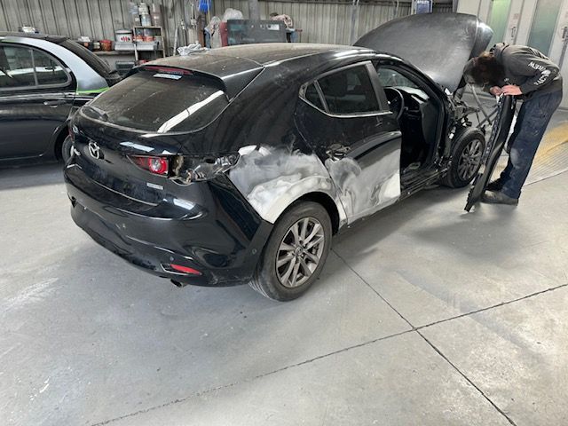 Black Tesla in a garage with rear and side damage, hood open, while a mechanic inspects it — Westside Panels & Towing in Prospect Vale, TAS