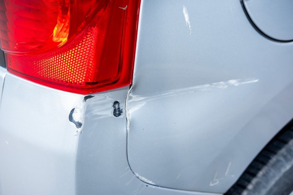 Close-up of a silver car’s rear corner with damage near the red taillight and dented bumper area — Westside Panels & Towing in Prospect Vale, TAS