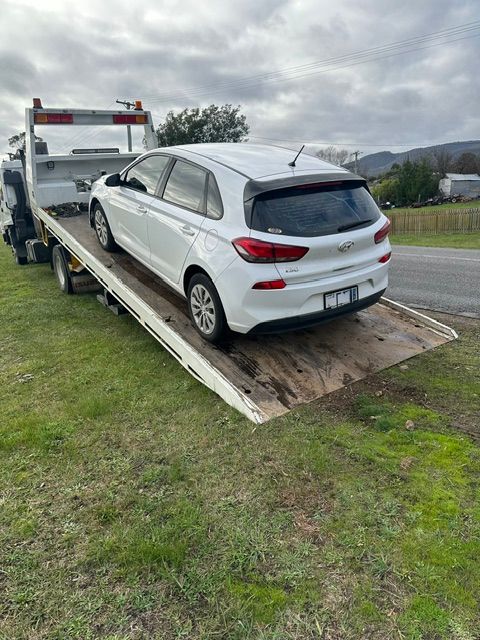 White hatchback on a flatbed tow truck ramp beside a road under cloudy skies - — Westside Panels & Towing in Prospect Vale, TAS