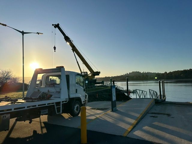 Crane truck by the waterfront at sunset, with a raised boom and dockside railings— Westside Panels & Towing in Prospect Vale, TAS