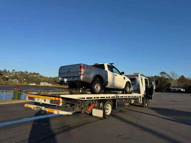 Tow truck hauling a damaged white pickup truck on a flatbed in a parking  — Westside Panels & Towing in Prospect Vale, TAS