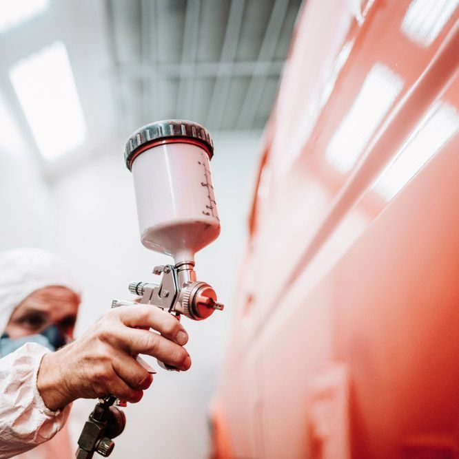 A Man Spray Painting A Repaired Panel on a Red Car — Westside Panels & Towing in Prospect Vale, TAS