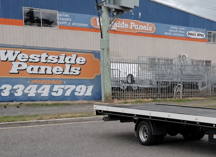Westside Panels building with orange-gray exterior and a trailer parked in front.— Westside Panels & Towing in Prospect Vale, TAS