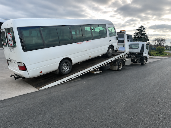 White minibus loaded on a tow truck on a road near an intersection — Westside Panels & Towing in Prospect Vale, TAS