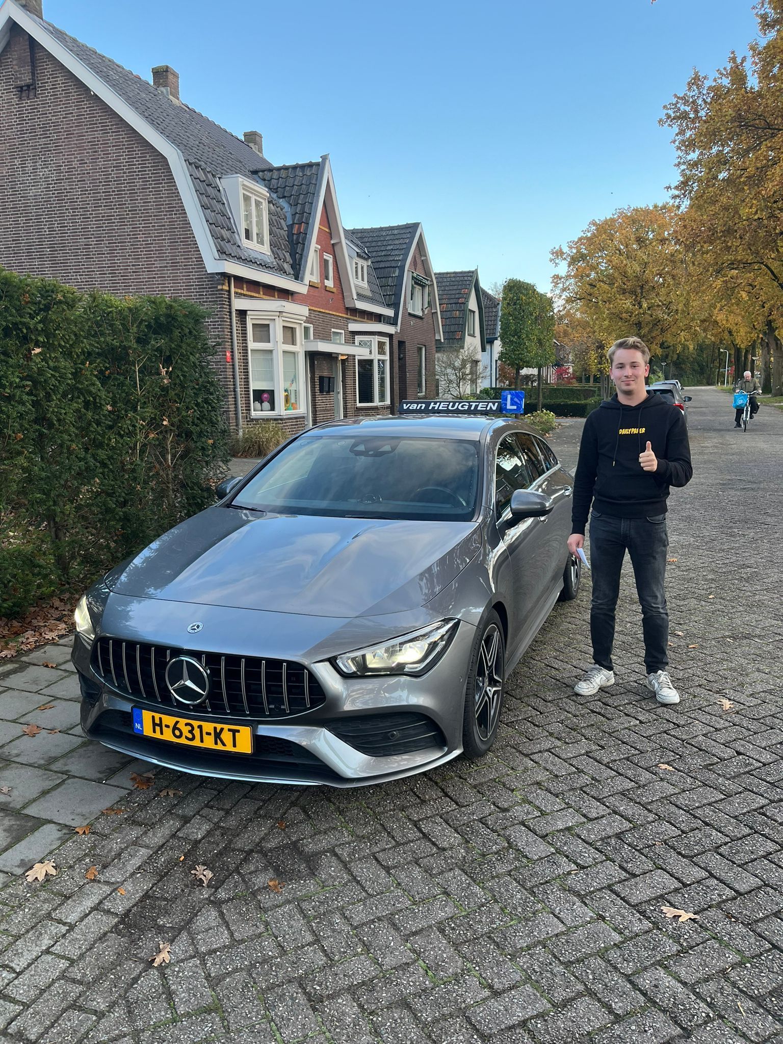 Een man staat naast een grijze Mercedes op een straat met kinderkopjes in een woonwijk.