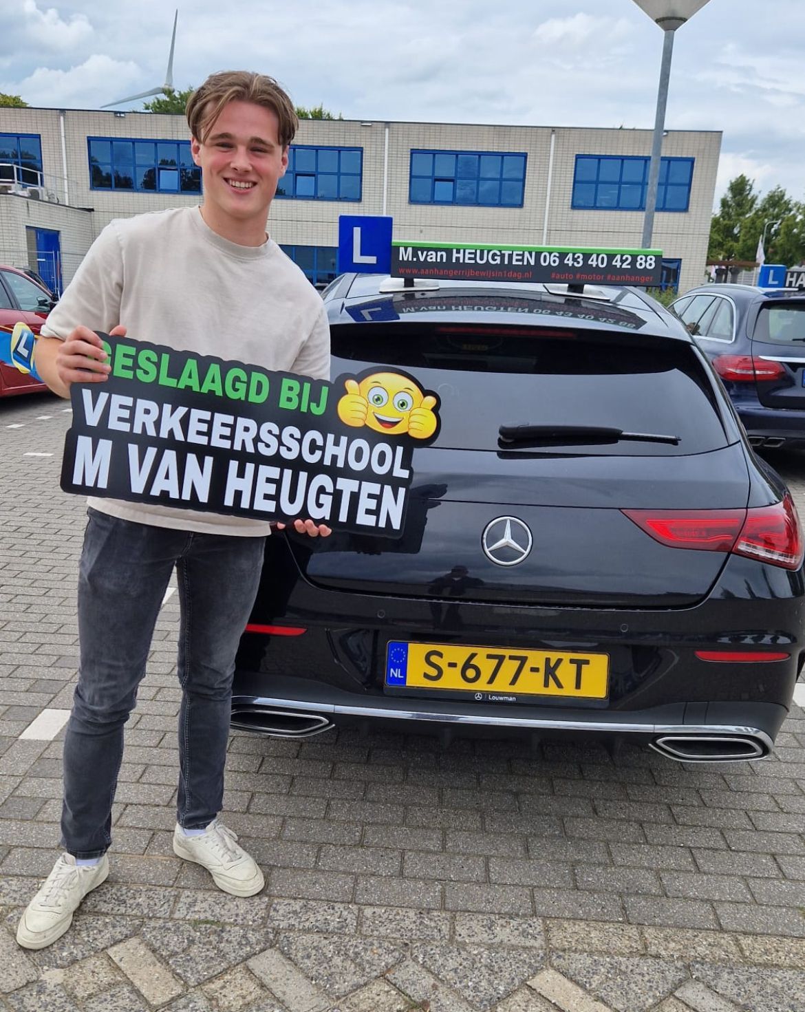 Jongeman met een bord van een rijschool voor een zwarte Mercedes met een Nederlands kenteken.