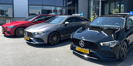 Drie geparkeerde Mercedes-auto's voor een autodealer, waaronder een rode, een zilveren en een zwarte uitvoering.