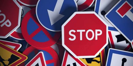 Diverse verkeersborden, waaronder een rood STOP-bord en blauwe richtingpijlen, liggen op een hoop.