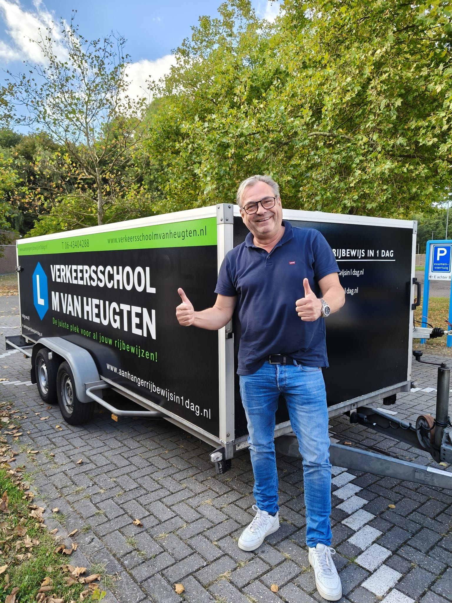 Een zwart-groene lesauto van de rijschool staat geparkeerd op een weg onder een bewolkte hemel.
