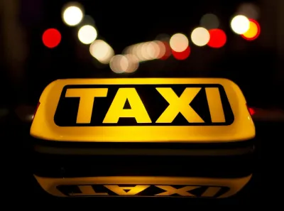 Verlicht geel TAXI-bord op het dak van een auto 's nachts met wazige stadslichten op de achtergrond.