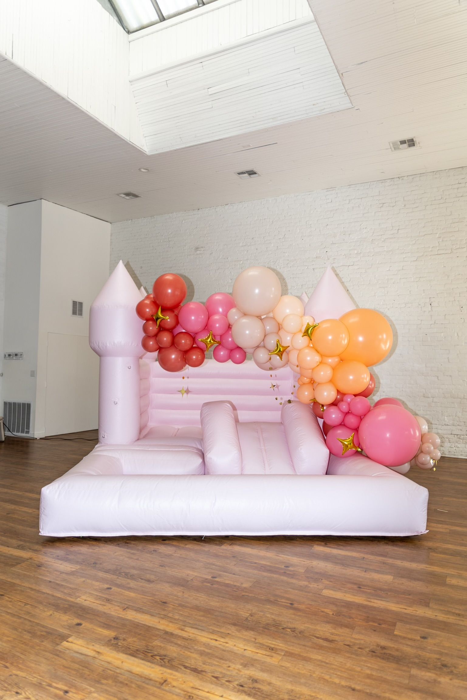 A pink bouncy castle decorated with pink and orange balloons is sitting on a wooden floor.