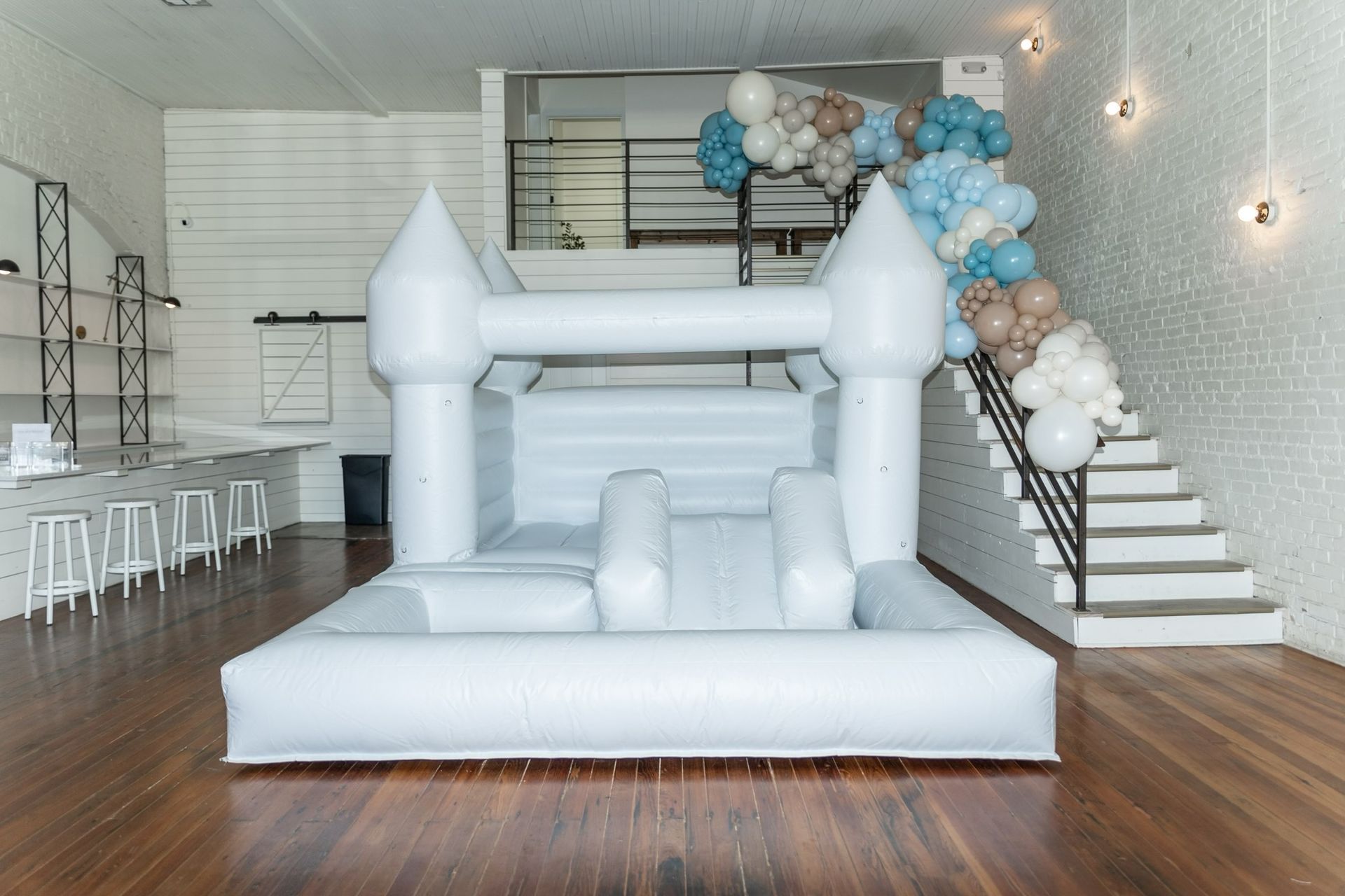 A white bouncy castle in a room with stairs and balloons